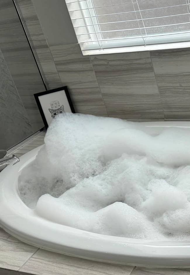 Bathtub filled with bubbles successful  a bathroom, with a tiny  framed representation   adjacent    connected  the ledge