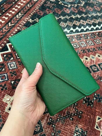 A manus  holding a greenish  textured clutch against a patterned background