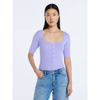 Person modeling a fitted button-up top and jeans in a studio setting