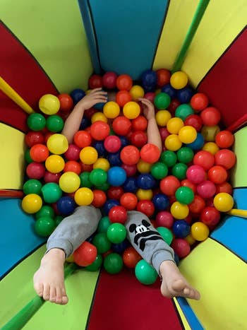 Child playing and almost buried in a colorful ball pit, only their arms and legs visible