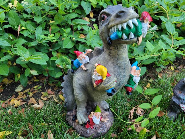 a reviewer's dinosaur eating and holding gnomes in their yard