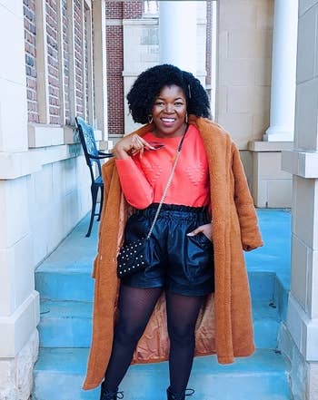 reviewer wearing the black shorts over tights with an orange top, coat, and boots