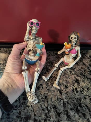 Skeleton figurines successful swimsuits holding cocktails, 1 held successful a hand. Perfect for quirky, beach-themed décor oregon Halloween fun
