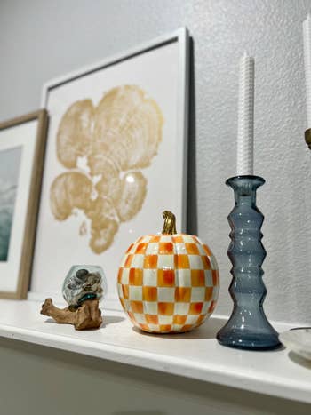 Pumpkin decor with checkered signifier   beside bluish  candle holder and framed creation  connected  a shelf, suitable for autumn-themed buying  articles