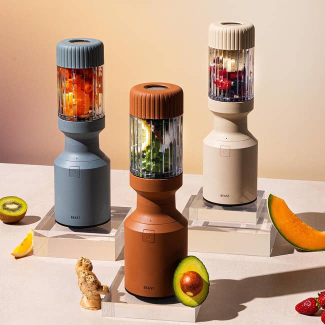 Four stylish countertop blenders with whole fruits and vegetables displayed around them