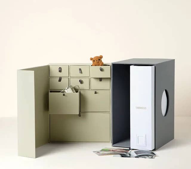 the gray and tan baby keepsake library with different compartments, scattered photos, and a mini teddybear 