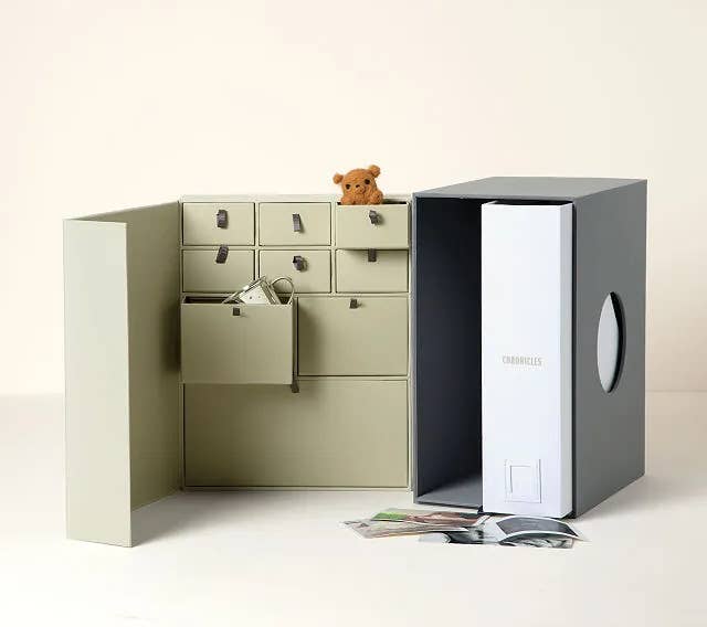 the gray and tan baby keepsake library with different compartments, scattered photos, and a mini teddybear 