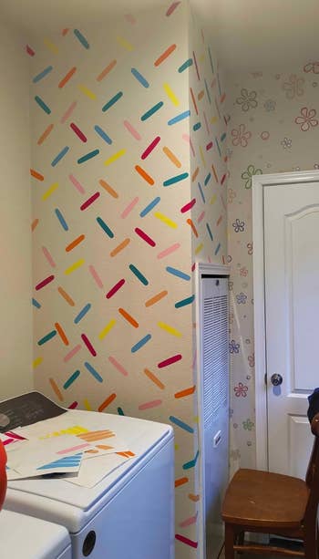 Laundry country   with colorful sprinkle signifier   connected  the wall, a chair, a washer and dryer, and overgarment   swatches connected  the dryer
