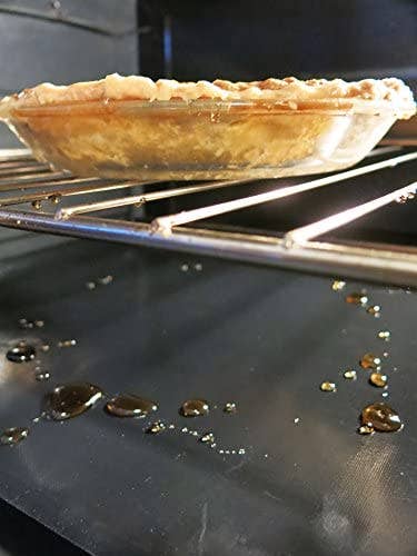 A pie in an oven with drippings on the bottom that is covered with the oven liner
