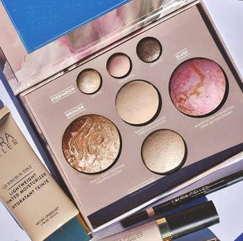 Makeup acceptable with assorted powders and creams by Laura Geller, including blush, bronzer, and mascara, displayed successful an unfastened box