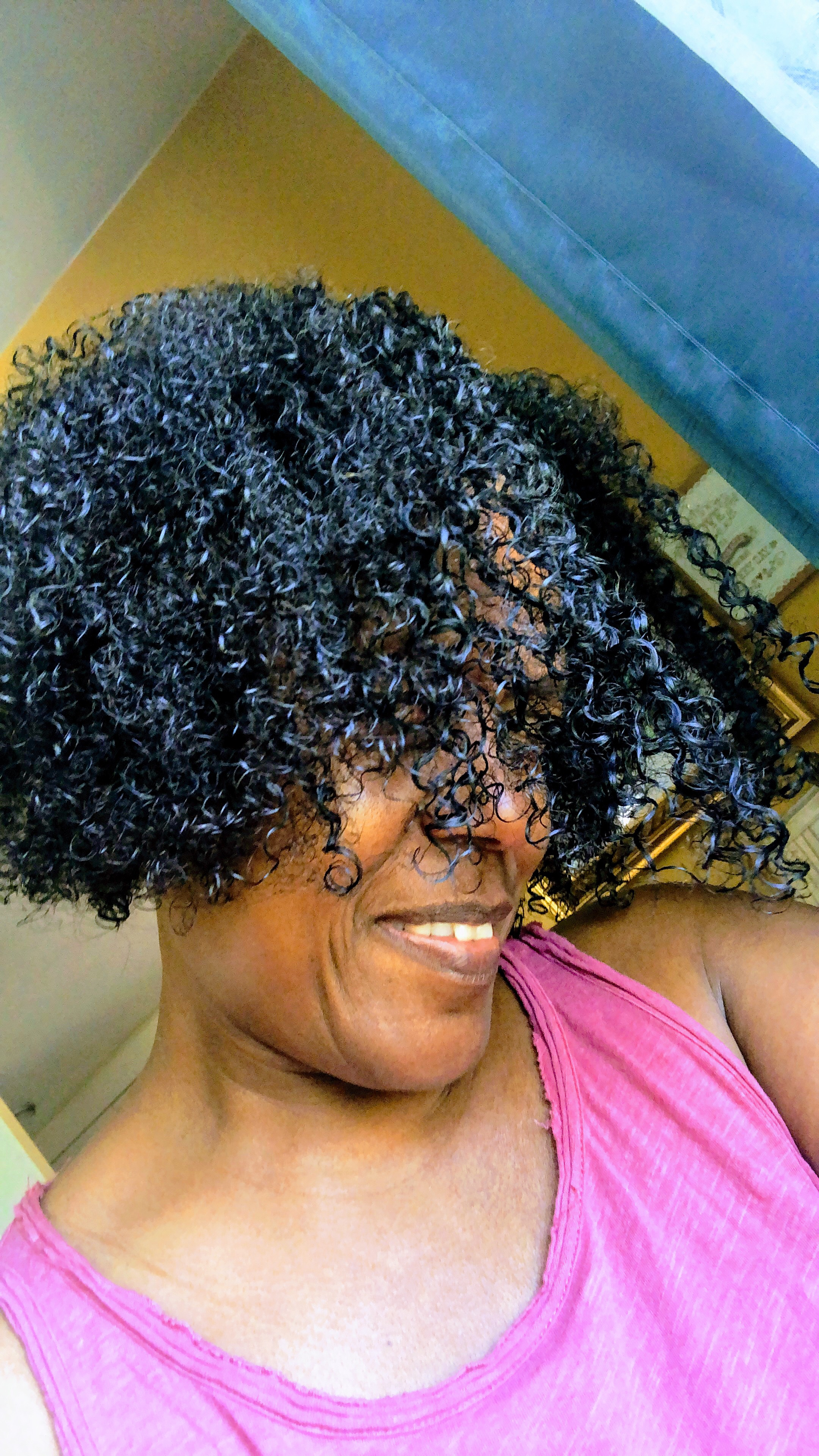 Person with curly hair smiling, wearing a casual sleeveless top
