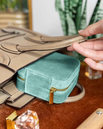 Model showing light blue jewelry box product inside beieg purse