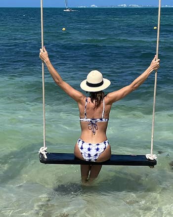 reviewer wearing straw hat with bathing suit while sitting on a swing over water