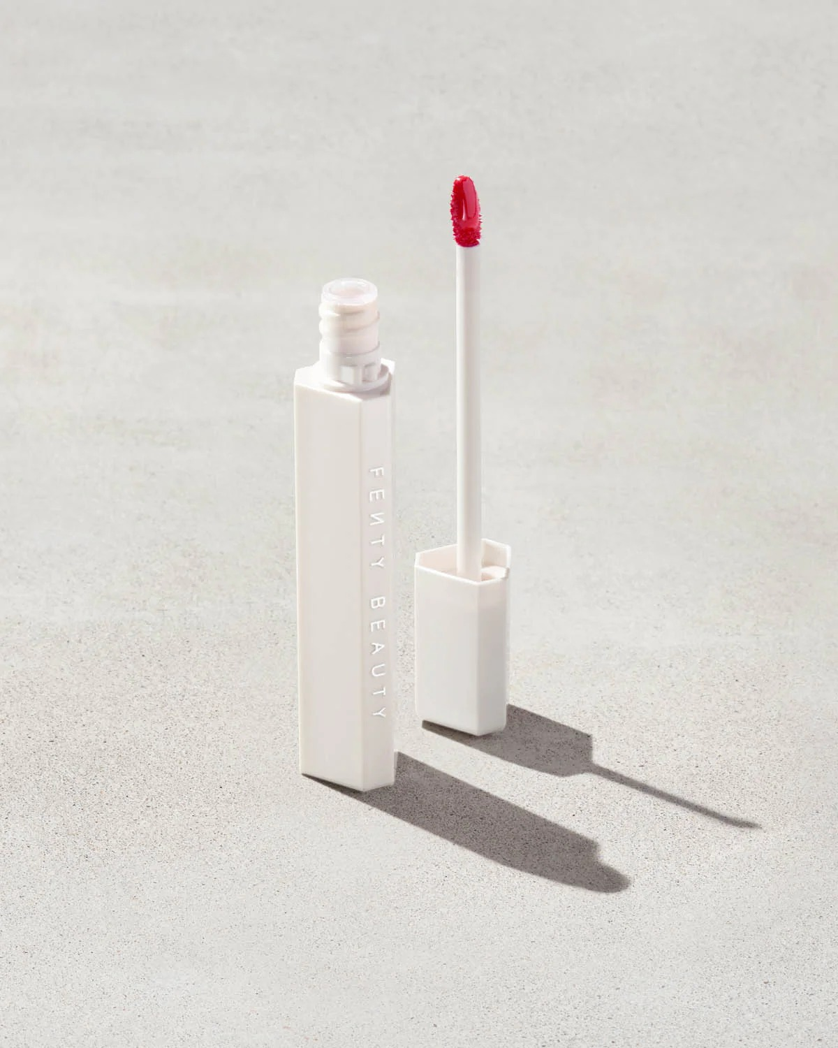 Tube of Fenty Beauty articulator  gloss with wand, unfastened  connected  a neutral background, showcasing sleek packaging