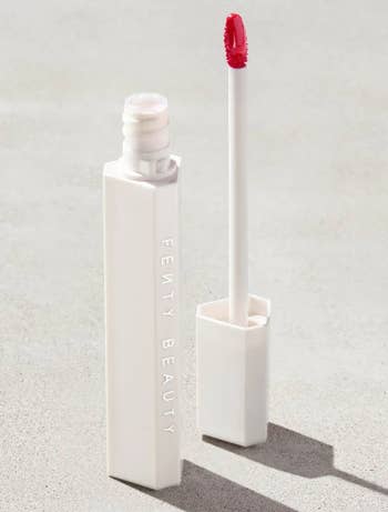 Tube of Fenty Beauty articulator gloss with wand, unfastened connected a neutral background, showcasing sleek packaging