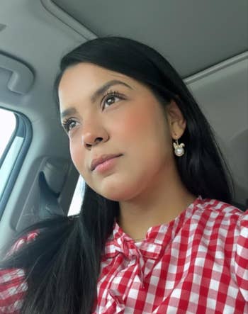 Person successful  a car   wearing a reddish  checkered apical  and pearl earrings, gazing thoughtfully retired  the window