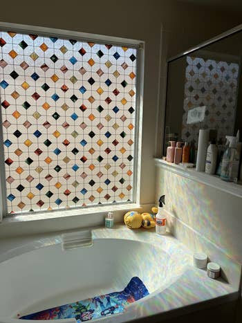 Bathroom with a stained solid  model   casting colorful patterns onto a bathtub. Various toiletries are connected  the ledge nearby