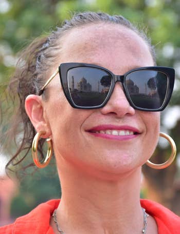 Person smiling with ample  sunglasses reflecting a celebrated  monument. They deterioration  hoop earrings and a casual top