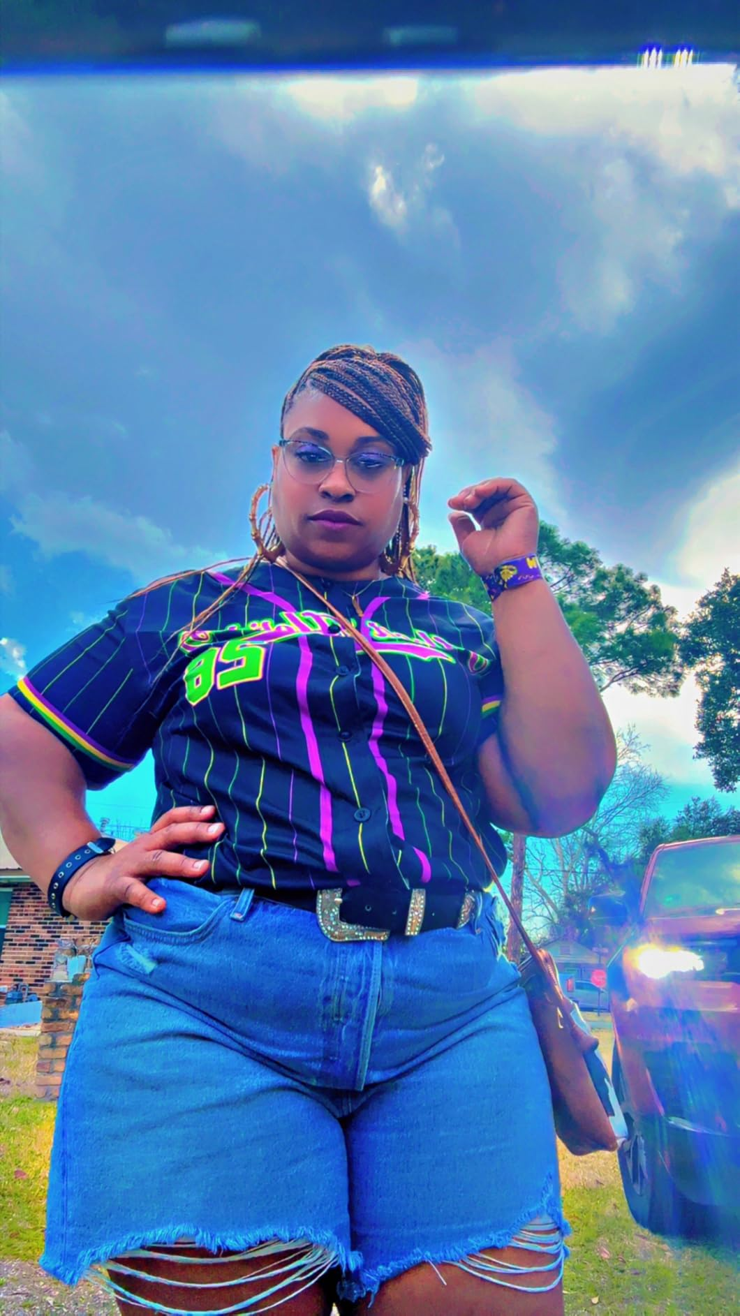Person outdoors successful  a casual outfit with a patterned shirt, denim shorts, belt, and a crossbody bag, striking a assured  pose