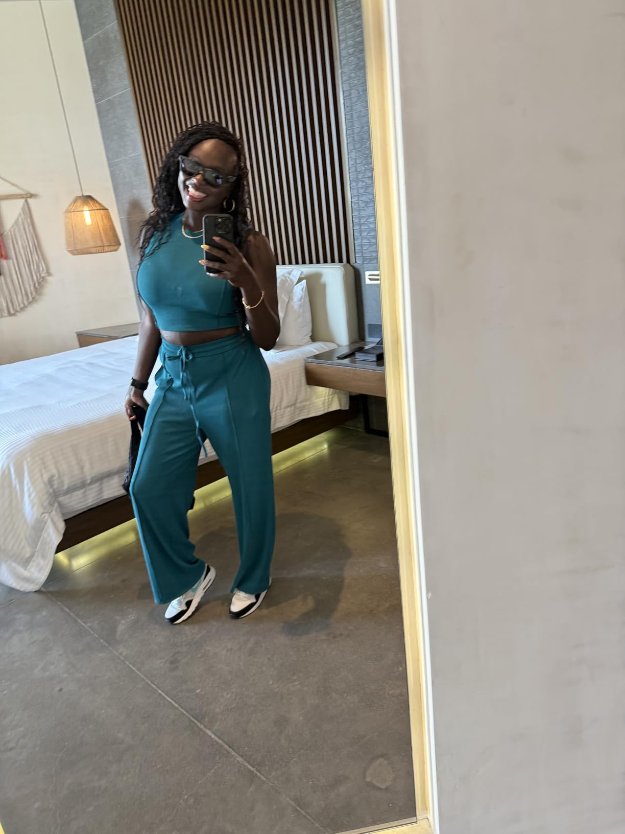Woman successful  a reflector  selfie wearing a sleeveless apical  and escaped   pants with sneakers. She holds a telephone  and smiles, with a relaxed, casual style