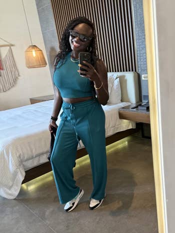 Woman successful a reflector selfie wearing a sleeveless apical and escaped pants with sneakers. She holds a telephone and smiles, with a relaxed, casual style