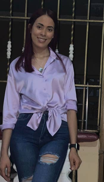 a reviewer in a knotted lavender satin blouse and distressed jeans, smiling, standing indoors