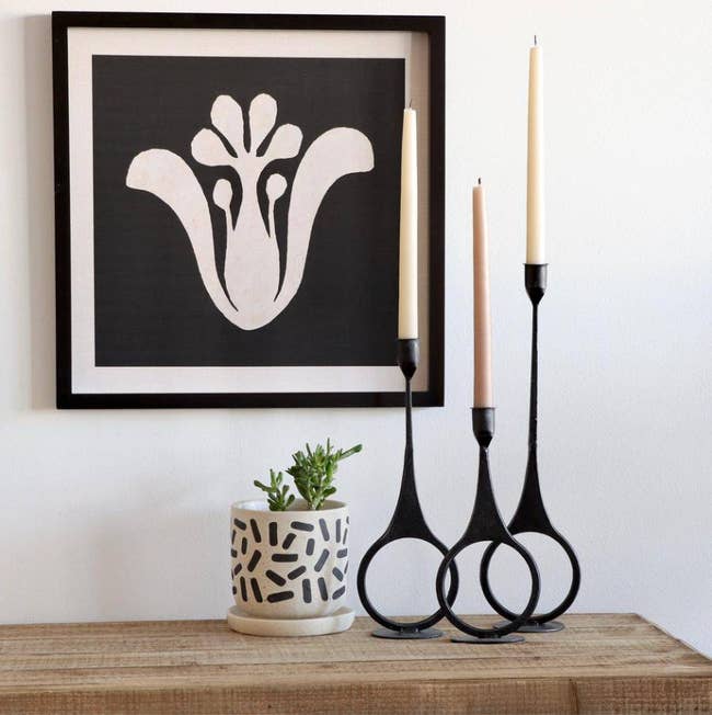 the set of three candle holders sitting on a table beside a plant