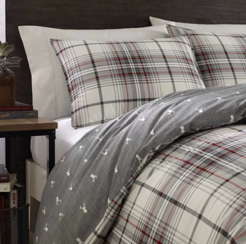 Close up of comforter with gray side and white deer pattern next to brown side table