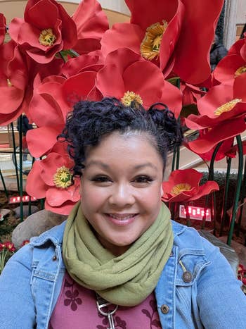 Person smiling successful  beforehand   of ample  artificial flowers, wearing a denim overgarment   and greenish  scarf