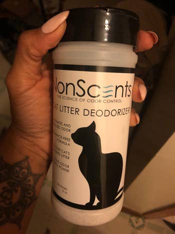 Person holding a NonScents Cat Litter Deodorizer bottle with a cat silhouette label, aimed at neutralizing litter odors
