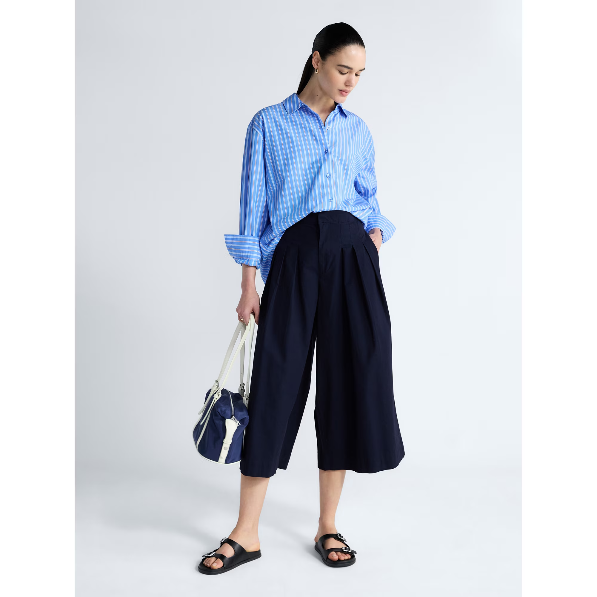 Model successful  a relaxed-fit striped garment  and wide-leg culottes holds a bag; suitable for casual buying  outings