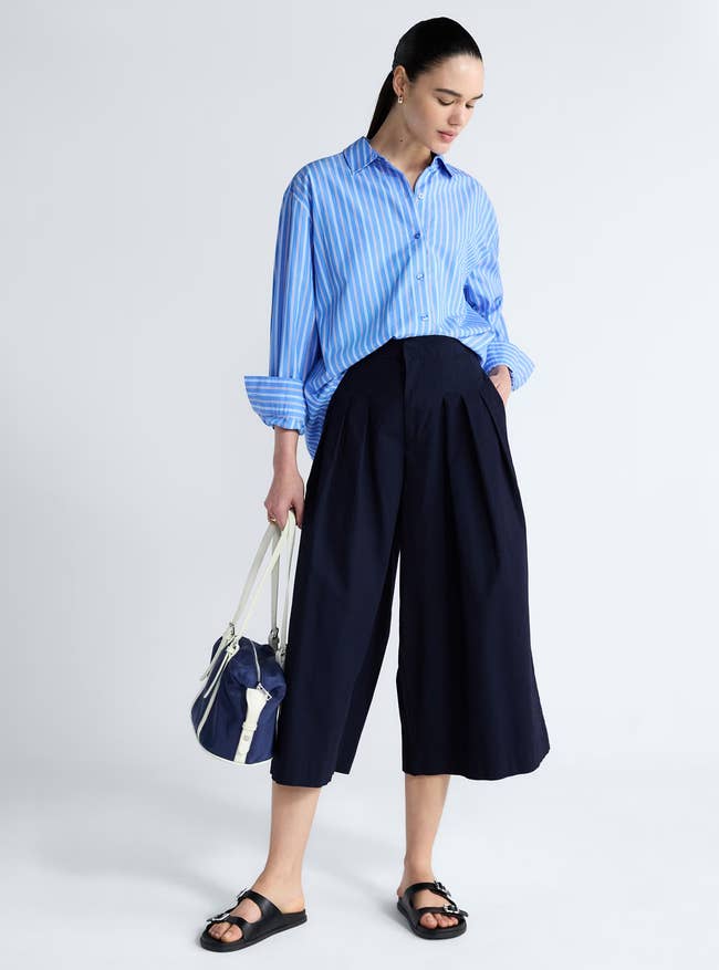 Model successful a relaxed-fit striped garment and wide-leg culottes holds a bag; suitable for casual buying outings