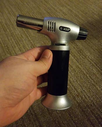 Entertainmment news A hand holding a S-400 culinary torch with a black grip and silver accents 