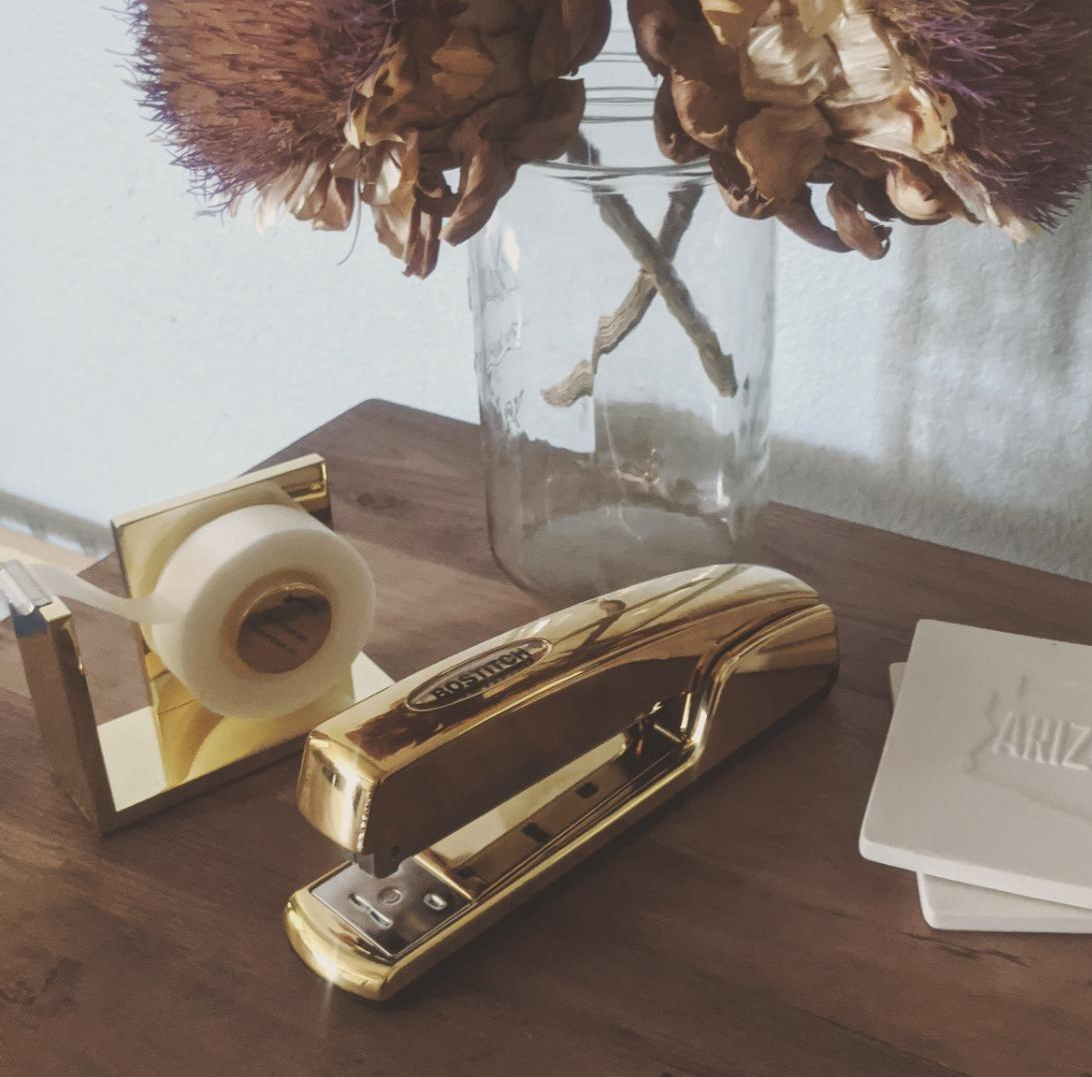 reviewer photo of the gold stapler on a desk next to a tape dispenser and flower vase