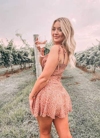 reviewer posing in pink romper holding wine glass