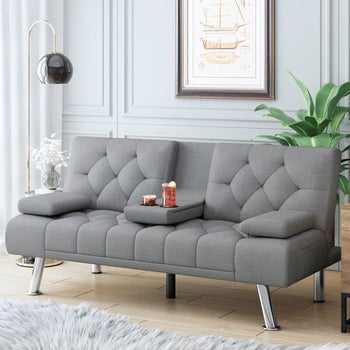 a grey futon in an upright position with a middle cushion pulled down to reveal cupholders