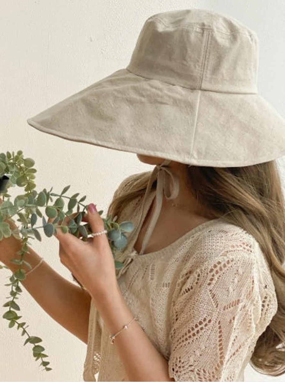 Model in a beige bucket hat obscuring their face with a tie at the chin 