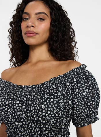 Woman wearing an off-shoulder, floral-patterned top, looking confidently at the camera