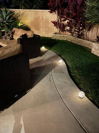 Outdoor patio with wicker furniture and solar garden lights on a curved pathway. The area is landscaped with plants and a stone retaining wall in the background