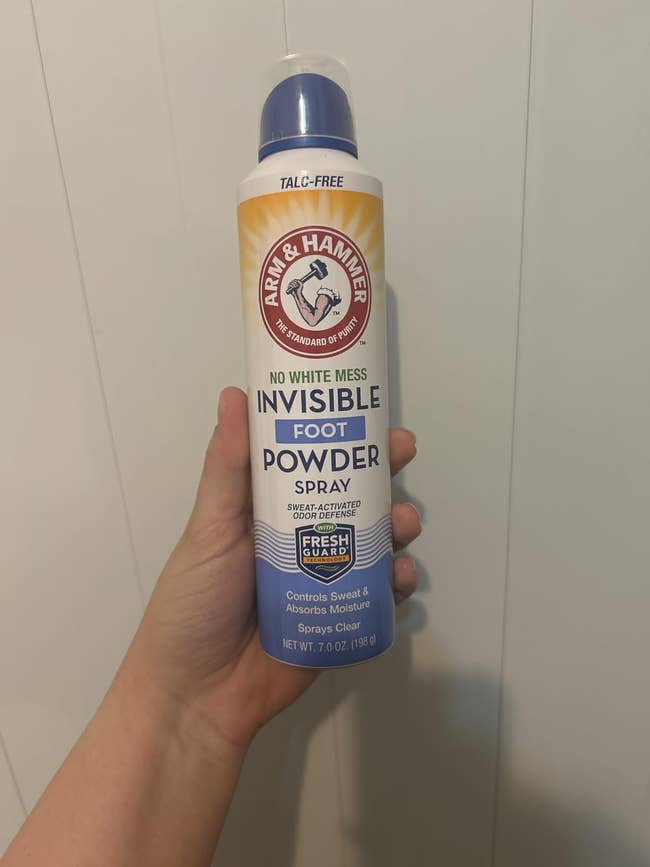 Hand holding Arm & Hammer Invisible Foot Powder Spray bottle, labeled arsenic talc-free and designed to power sweat and sorb moisture