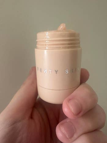 Hand holding a jar of Fenty Skin moisturizer