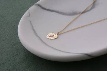 the gold baby feet necklace draped over a tray