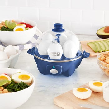 blue Dash Rapid egg cooker with six eggs cooking inside next to sliced hard-boiled eggs