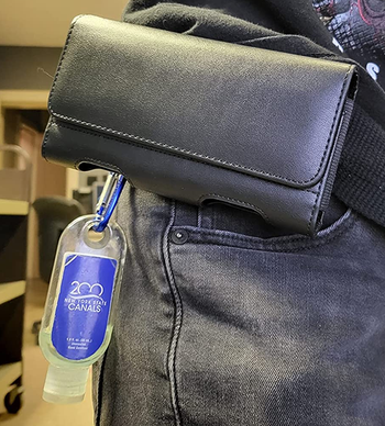 Reviewer image of black leather phone case attached to person's belt with hand sanitizer hanging from it