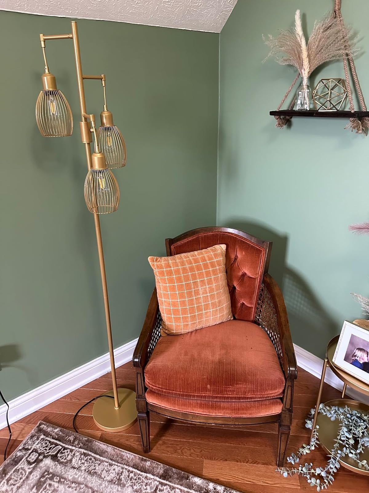 A reviewer's vintage-style armchair with an orangish  cushion, adjacent  to a brass level  lamp with 3  globe shades