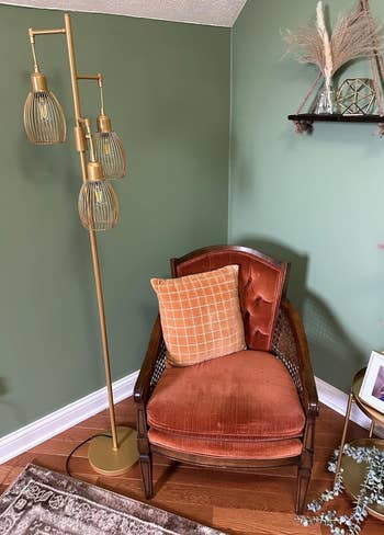 A reviewer's vintage-style armchair with an orange cushion, next to a brass floor lamp with three globe shades