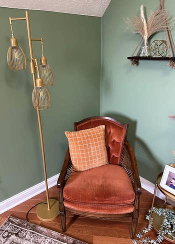 A reviewer's vintage-style armchair with an orangish cushion, adjacent to a brass level lamp with 3 globe shades
