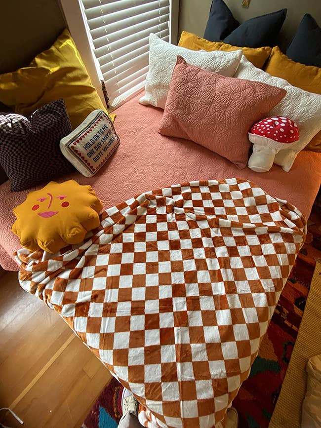 reviewer image of the orange checkered blanket on the corner of a bed