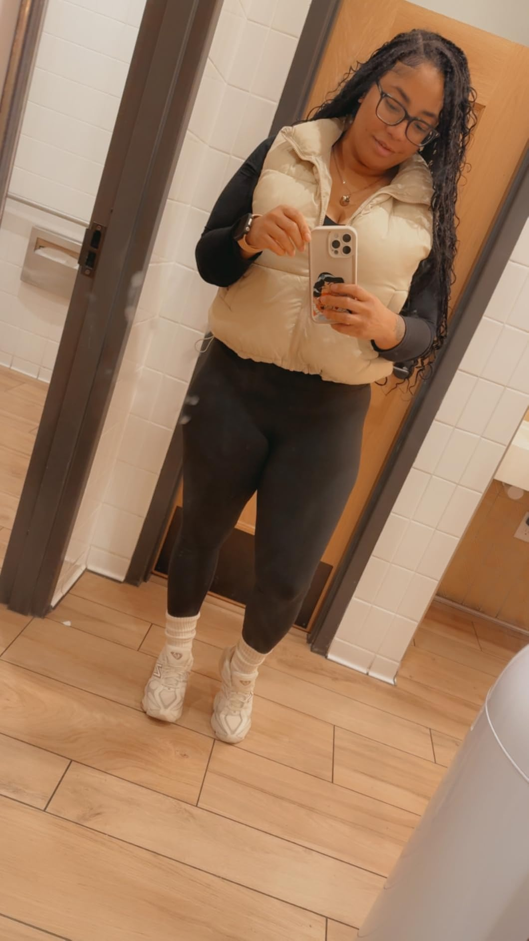 A idiosyncratic   poses successful  a restroom reflector  wearing a sleeveless puffer vest, long-sleeve top, leggings, and sneakers