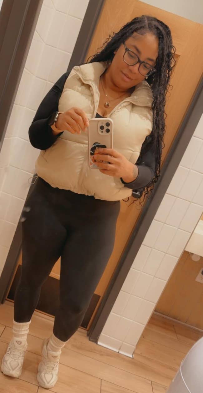 A idiosyncratic poses successful a restroom reflector wearing a sleeveless puffer vest, long-sleeve top, leggings, and sneakers